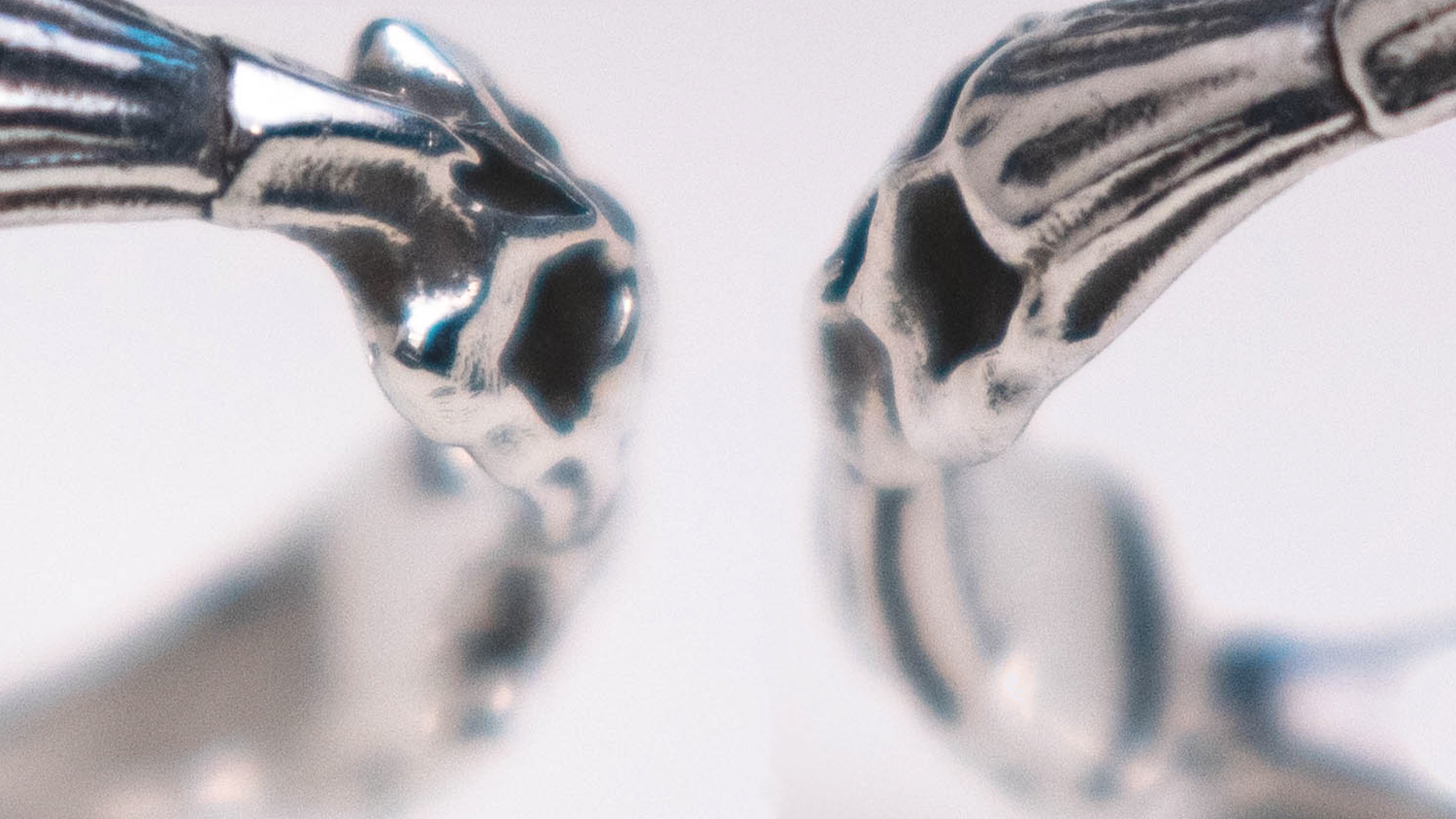 Close-up of two sterling silver skull stack rings facing each other, showing detailed skull and bone band craftsmanship by Ian's Objects