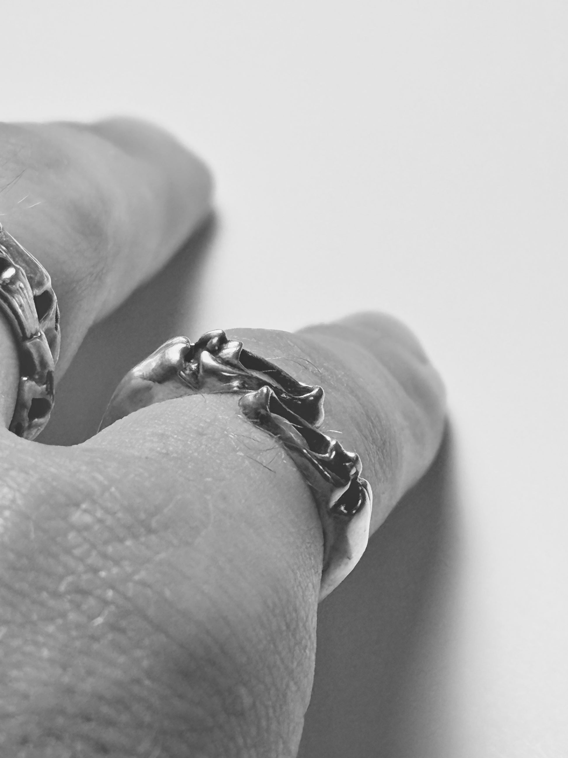 Sterling silver screaming faces bypass ring worn on pinky finger alongside skull stack rings, showing sculpted detail in black and white lifestyle photo